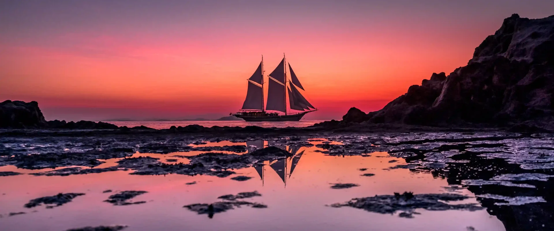 A phinisi sailing boat departing at sunset, sails raised